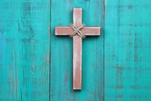 Wooden cross hanging on antique teal blue wall